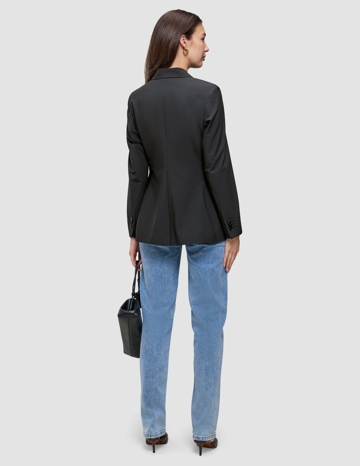 Bakfra-bilde av en person som har på seg en svart Women’s Avira Blazer Black, lyseblå jeans og mørke høyhælte sko, og som holder en håndveske.